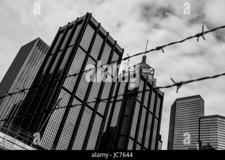 Point de vue noir et blanc d'un site de construction à Hong Kong avec d'autres grands bâtiments en arrière-plan et une clôture en fil barbelé au premier plan. Banque D'Images