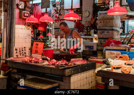 Impression photo d'un poissonnier de fileter un poisson sur une planche à découper ronde dans sa cabine à l'étroit dans un marché traditionnel à Macao. Banque D'Images