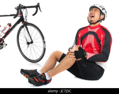 Cycliste asiatique est tombé de vélo à l'articulation du genou blessé, douleur à l'expression du visage et assis sur le plancher, isolé sur fond blanc. Banque D'Images