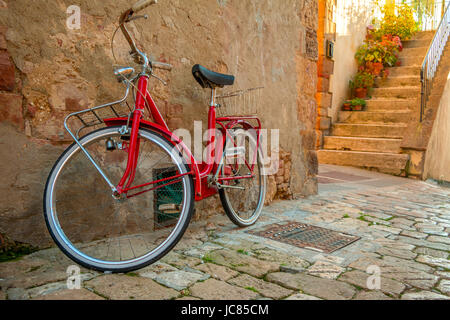 L'Italie. Pienza. Un vélo rouge se dresse sur la rue étroite de la vieille ville près du mur de pierre de l'édifice Banque D'Images