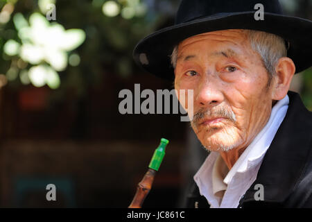 Shaxi, Yunnan, Chine - 21 novembre 2010 : old chinese reposant sur la porte de son chalet fumant une pipe dans le village shaxi Banque D'Images