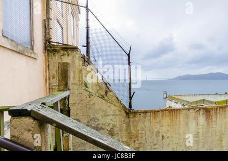 La clôture autour de la cour de récréation sur l'île pénitencier d'Alcatraz, maintenant un musée, à San Francisco, Californie, USA. Une vue de l'île au trésor et le pont de la baie de l'Cellhouse. Banque D'Images