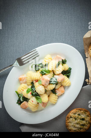 Une cuisine italienne traditionnelle avec une assiette de pâtes, gnocchi ou boulettes, faites avec de la semoule et servi avec le basilic et les cubes de saumon grillé, vue du dessus sur gris avec copyspace Banque D'Images