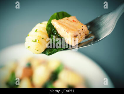 Forkful de saumon grillé, gnocchi basilic italien et assaisonné avec des herbes et épices suspendu au-dessus de la plaque avec selective focus Banque D'Images