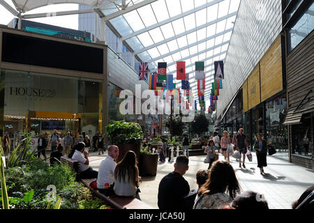 Transporter des sacs de shopping shopping ; les gens se détendre sur les bancs dans le centre commercial Westfield Stratford City ; World flags hanging le long du corridor Banque D'Images