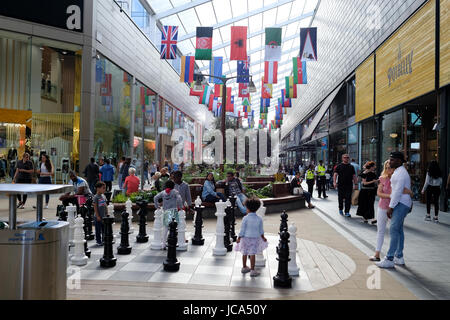 Des enfants jouent au jeu d'échecs dans la région de Westfield Stratford City Shopping Centre ; monde drapeaux sont suspendues au-dessus le long du corridor Banque D'Images