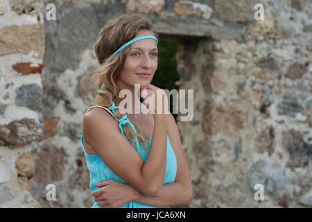 Young blonde woman wearing turquoise haut standing contre mur en pierre médiévale et à l'écart Banque D'Images