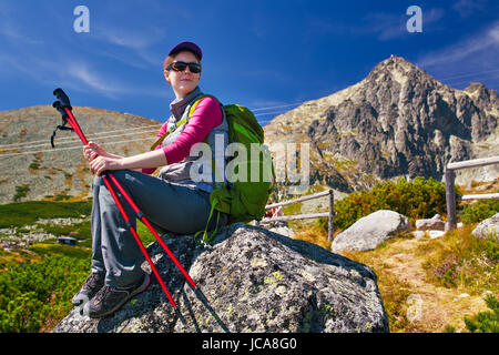 Jeune femme avec sac à dos vert tourisme et des poteaux assis sur de hautes montagnes background Banque D'Images