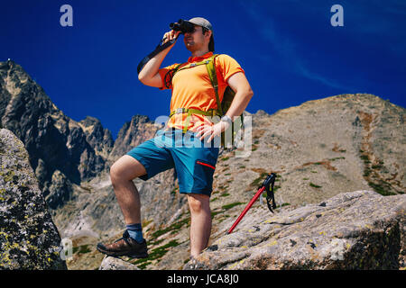 Jeune homme avec sac à dos vert touristiques à la recherche de jumelles sur de hautes montagnes Banque D'Images