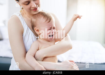 Jeune femme avec bébé qui pleure sur les mains. Coloris blanc brillant. Banque D'Images