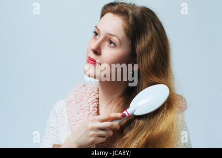 Jeune femme blonde en peignoir comb cheveux après le lavage. Sur fond blanc. Banque D'Images