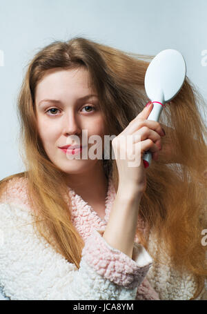 Jeune femme blonde en peignoir comb cheveux après le lavage. Sur fond blanc. Banque D'Images