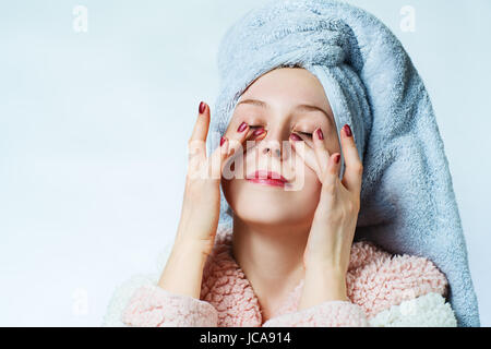Jeune femme avec peignoir et serviette faisant massage sous les yeux. Spa beauté portrait. Banque D'Images