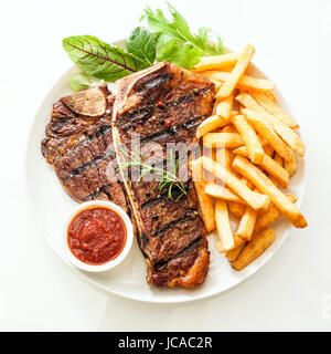 T-bone grillé ou steak d'aloyau assaisonnés avec le romarin et servi avec frites dorées, salade d'Herbes et légumes frais une tomate trempette, high angle view on white Banque D'Images