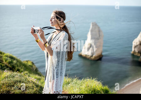 Jeune femme habillée dans le style hippie de photographier le paysage magnifique debout sur la côte rocheuse en France Banque D'Images