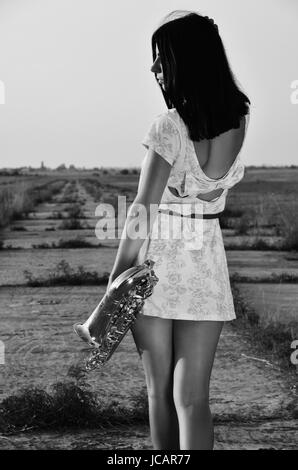 Une fille avec son dos dans la robe près de la hanche tient le saxophone. Photographie en noir et blanc Banque D'Images