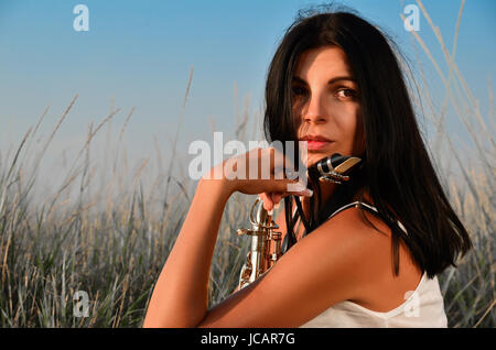 Une belle brune est assise dans un blé avec un saxophone et regarde ailleurs Banque D'Images