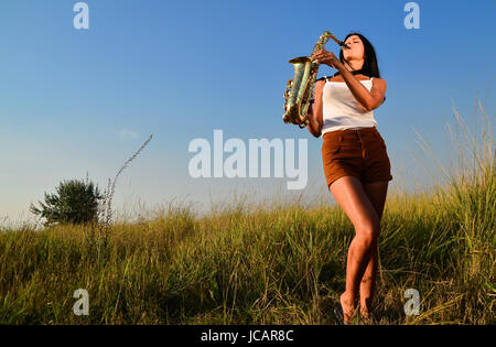 Femme à jouer du saxophone dans la nature sur fond vert Banque D'Images