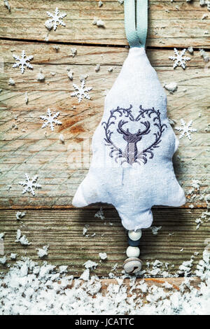 Textiles brodés à la main décoration d'arbre de Noël avec un renne et grelot suspendu à un cadre rustique en bois avec fond texturé et flocons de neige de l'hiver Banque D'Images