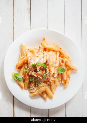 Vue de dessus d'une assiette santé italien de pâtes penne au basilic, sarriette sauce épicée et parmesan râpé sur les planches de bois blanc rustique avec copyspace Banque D'Images