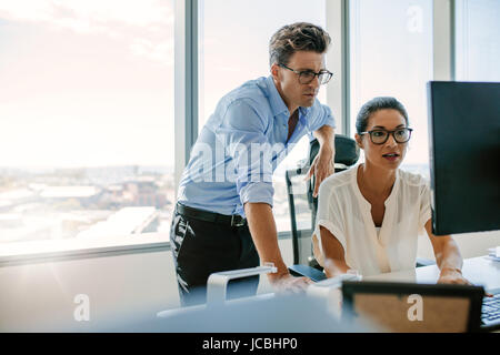 Asian businesswoman assise à son bureau et de travail sur ordinateur avec un collègue masculin par permanent. Deux professionnels qui travaillent ensemble à l'Offic Banque D'Images