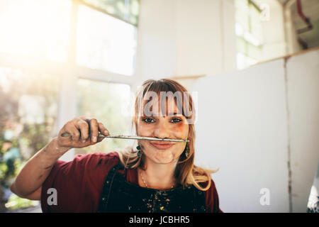 Close up of young woman artist avec le pinceau. Femme painter holding brosse entre le nez et la bouche. Banque D'Images