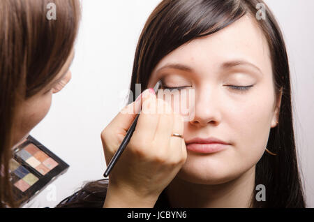 Offres d'artiste de maquillage maquillage sur le visage du modèle. Elle peint les ombres de la paupière supérieure modèle. Banque D'Images