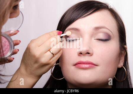 Offres d'artiste de maquillage maquillage sur le visage du modèle. Elle peint les ombres de la paupière supérieure modèle. Banque D'Images