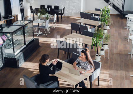 Happy businesswoman talking to businesswoman in office. Deux femmes assises à table avec des ordinateurs portables et de travail. Banque D'Images