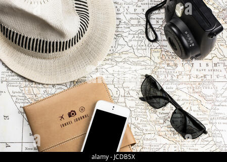 Concept de voyage avec des essentiels de voyage arrangés avec une carte ancienne, appareil photo instantané, téléphone, lunettes de soleil, et chapeau blanc, préparation d'un voyage Banque D'Images