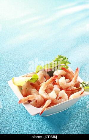 Crevettes crevettes roses fraîches ou apéritif servi avec des tranches de citron et les légumes verts pour une étape gourmande à un repas de début de coquillages, sur bleu avec copyspace Banque D'Images