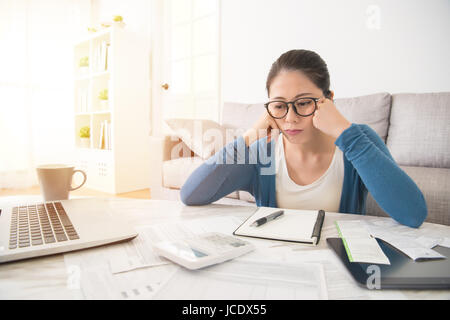 Triste belle course mixte chinois asiatique femme regardant les factures impayées se sentent affligés assis sur le canapé dans le salon à la maison. l'intérieur et de la Banque D'Images