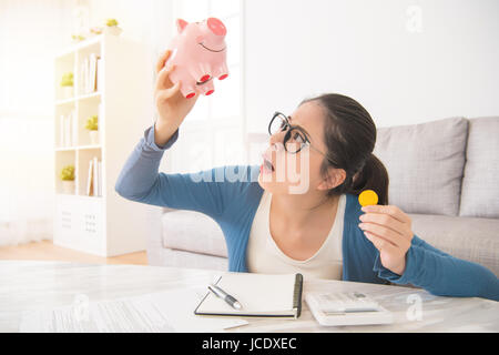 Jeune femme malheureuse de vider sa tirelire épargne avec moins d'attendre assis sur le canapé dans le salon à la maison et travaux ménagers domestiques d'intérieur. Banque D'Images