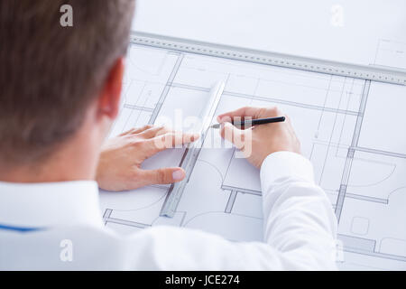 Close-up of Male Architect travaillant sur Blueprint At Desk Banque D'Images