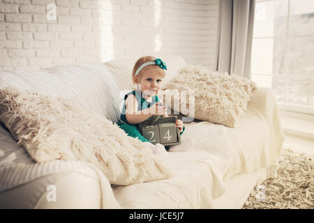 Joli gamin jouant sur canapé blanc à l'intérieur. Belle petite fille en blanc télévision moderne. Banque D'Images