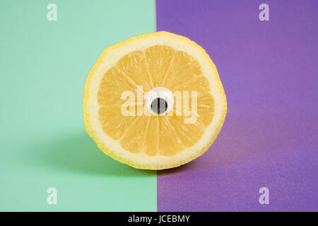 La photographie de la vie encore minime.un citron coupé en deux et porter les yeux comme une poupée cyclop bi pop. l'arrière-plan de couleur : violet et turquoise Banque D'Images