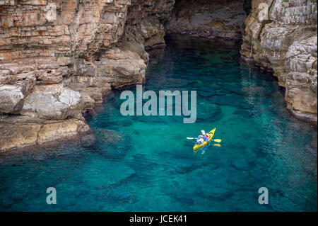 Vue depuis les falaises rocheuses de la kayakiste explorer les eaux limpides de la Méditerranée d'une anse de la côte de Dubrovnik, Croatie Banque D'Images