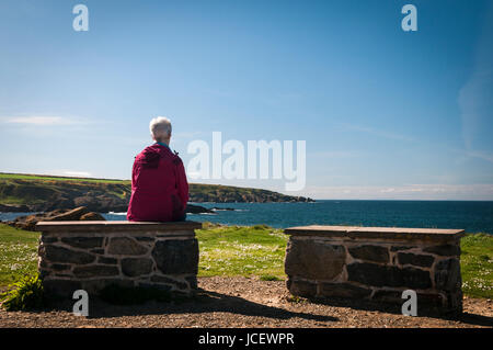 Dame portant une veste rouge à la recherche sur la mer à Portsoy, Banff et Buchan, Aberdeenshire, Scotland Banque D'Images