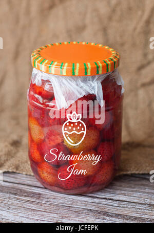 Confiture de fraise en pot avec ruban isolé sur fond de bois Banque D'Images