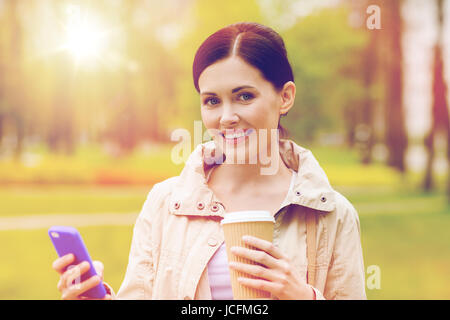 Smiling woman with smartphone et café dans park Banque D'Images