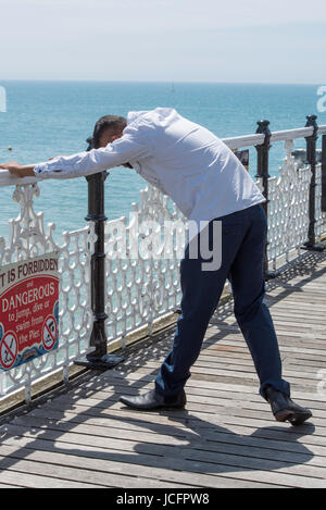 Un seul homme d'Asie s'étend ses bras sur les grilles sur le célèbre monument victorien, Brighton Palace Pier. La mer et le ciel bleu sont derrière lui. Banque D'Images