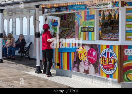 Palace Pier de Brighton sur une journée ensoleillée. Assis à l'ombre, les vacanciers sur la jetée victorienne tandis qu'un employé de magasin ouvre sa douce, wc séparés. Banque D'Images