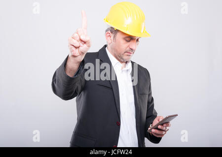 Portrait de l'architecte à occupé avec son smartphone portant un casque jaune sur fond gris Banque D'Images