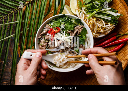 Soupe Pho Bo avec le boeuf et baguettes en mains mâles close-up Banque D'Images