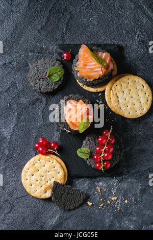 Pile de charbon noir et craquelins à grains entiers traditionnels avec le saumon fumé, fromage à la crème, salade verte et rouge des baies de cassis sur ardoise sur Banque D'Images