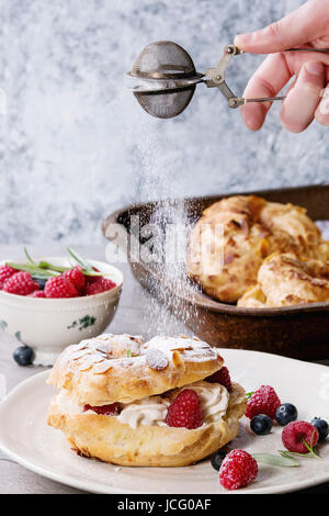 Remplir et vider des pâte à choux gâteau Paris Brest avec des framboises, l'amande, le sucre en poudre, le romarin sur la plaque et four avec des baies plus gra Banque D'Images