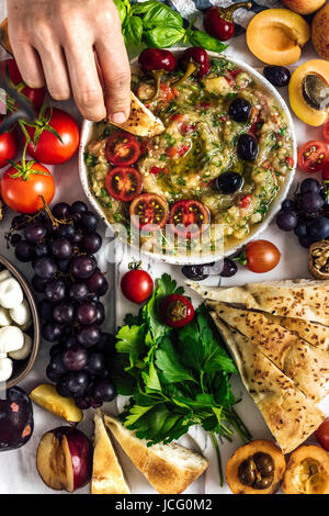 L'aubergine babaganoush avec poivron rouge et d'herbes sur une carte snack plein de fruits d'été photographiés en vue de dessus. Une femme est trempage d'un pain en Banque D'Images