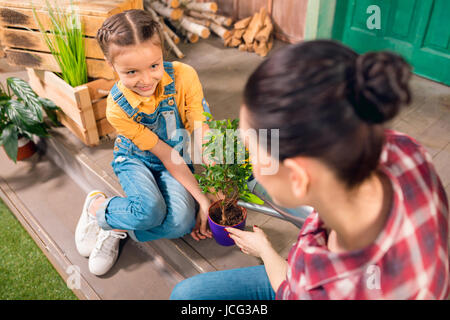 Portrait de Mère et fille souriant assis sur le porche et l'usine d'arrosage Banque D'Images