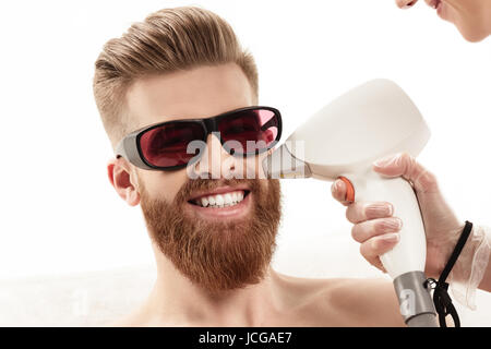 Jeune homme recevant des soins de la peau au laser sur le visage isolé sur blanc. de vie sain concept homme Banque D'Images