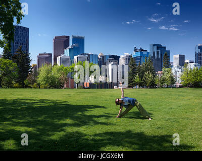 Young woman practicing Yoga in Banque Sunnyside Park sur une journée ensoleillée avec le Calgary city centre-ville en arrière-plan. Calgary, Alberta, Canada Banque D'Images